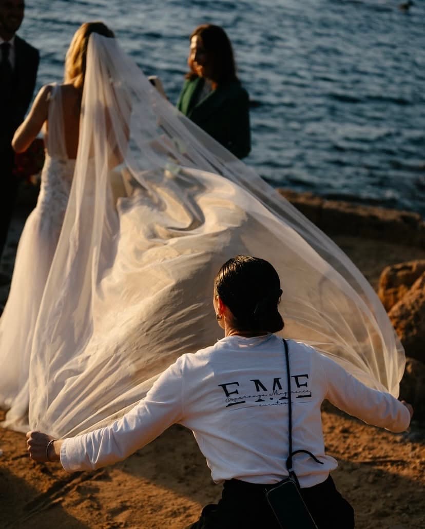 EME Eventos wedding planner adjusting the bride's veil at a seaside ceremony at sunset